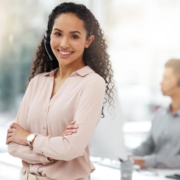 Portrait of a young call centre agent standing with her arms crossed in an office.