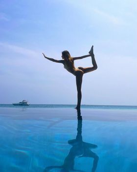 Beautiful slender woman in a swimsuit practicing yoga, Maldives, beautiful background, clean water, pool, sea and ocean.