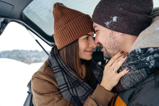 Lovely smiling couple sitting in car trunk in winter forest, close up