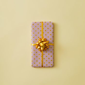 The mobile phone is gift-wrapped with a gold ribbon and a bow. Minimal modern gift concept.