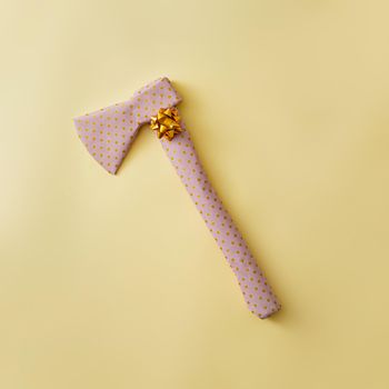 An ax wrapped as a gift with a golden bow. Joke concept and pastel color.