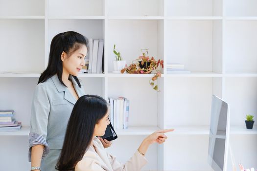 Consultation, discussion, marketing and investment concept, female employee holding folder and colleague pointing at a computer monitor to draw conclusions and assess investment risks for the company