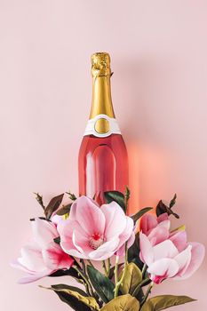 Full bottle of pink champagne with fresh flowers symbolic of love and romance over a pink background with copy space