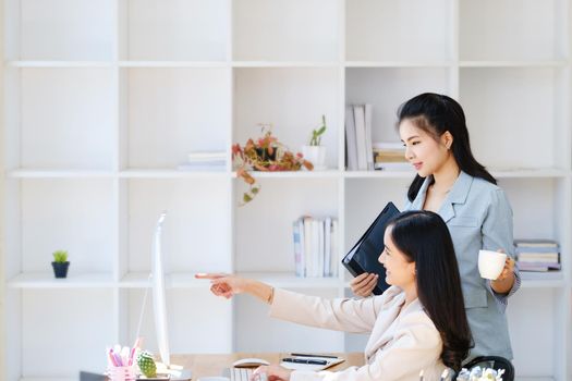 Consultation, discussion, marketing and investment concept, female employee holding folder and colleague pointing at a computer monitor to draw conclusions and assess investment risks for the company