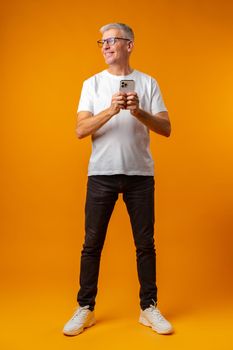 Senior smiling man using smartphone over yellow background, close up