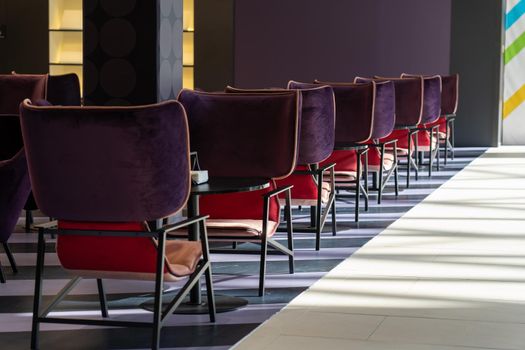 A row of tables with soft comfortable violet chairs for visitors to the food court of a modern shopping center. People admire the beautiful view during the meal.