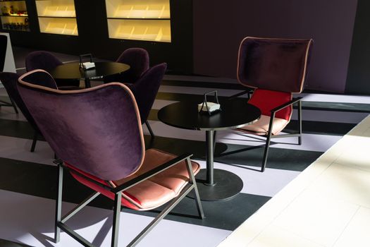 A row of tables with soft comfortable violet chairs for visitors to the food court of a modern shopping center. People admire the beautiful view during the meal.