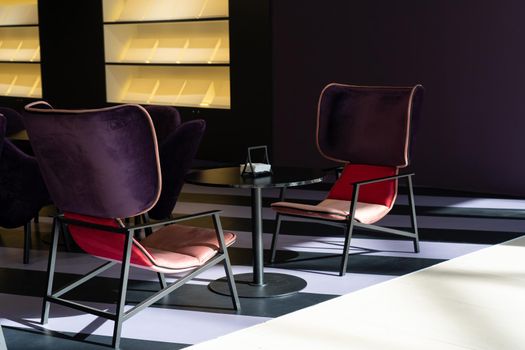 A row of tables with soft comfortable violet chairs for visitors to the food court of a modern shopping center. People admire the beautiful view during the meal.