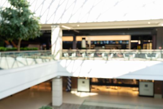 Blurred image interior of main hall shopping mall showing the floors and large skylight with natural light from glass roof. Glazed barrel vault spanning central axis, fashion boutique along corridor