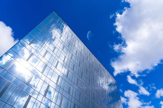 Architectural detail of the facade with multiple reflections of cloudy sky and the sun. Exterior of modern building. Architecture abstract background