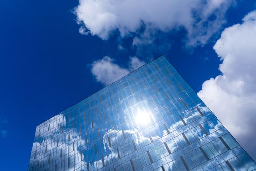 Architectural detail of the facade with multiple reflections of cloudy sky and the sun. Exterior of modern building. Architecture abstract background