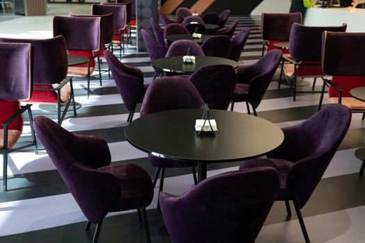 A row of tables with soft comfortable violet chairs for visitors to the food court of a modern shopping center. People admire the beautiful view during the meal.