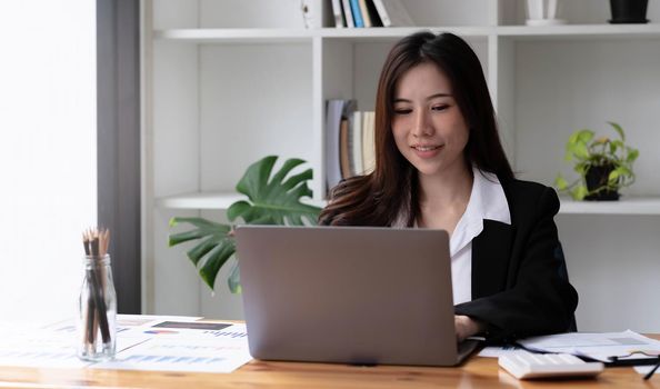 Business asian woman using laptop for do math finance on wooden desk in office, tax, accounting, financial concept.