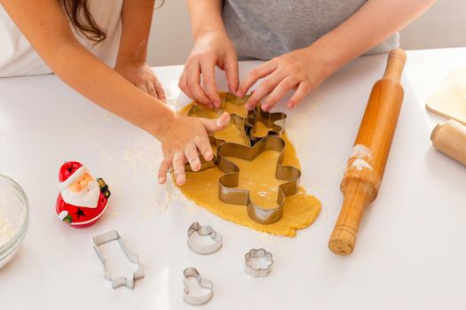 Children's hands, close-up, on a white table, cut out from the dough Christmas figured cookies in the form of a man, a Christmas tree and other figures. Top view