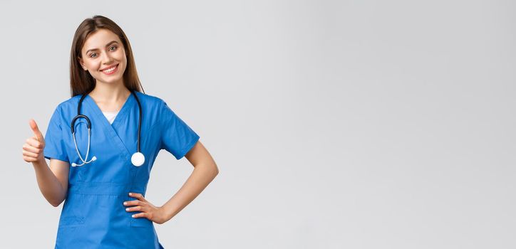 Medical workers, healthcare, covid-19 and vaccination concept. Attractive cheerful female nurse, doctor in scrubs showing support, recommend or advice medicine, show thumbs-up in approval smiling.