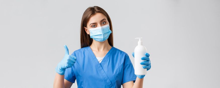 Covid-19, preventing virus, healthcare workers concept. Serious female nurse or doctor in blue scrubs, medical mask and gloves, recommend use soap or sanitizer against coronavirus infection.