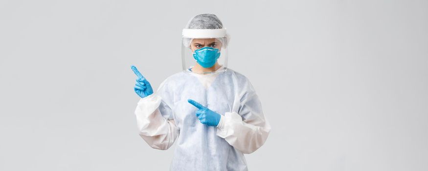 Covid-19, preventing virus, health, healthcare workers and quarantine concept. Angry frowning doctor or nurse in personal equipment, medical suit, respirator and gloves, pointing finger bad news.