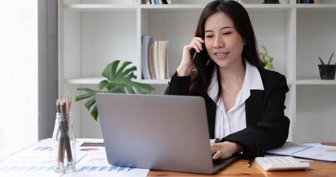 Business asian woman using smartphone for do math finance on wooden desk in office, tax, accounting, financial concept.