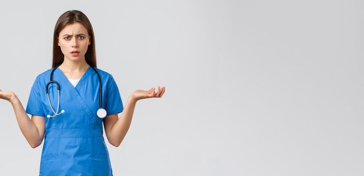 Healthcare workers, prevent virus, insurance and medicine concept. Confused and puzzled female nurse, doctor in blue scrubs, spread hands sideways and shrugging, cant understand.