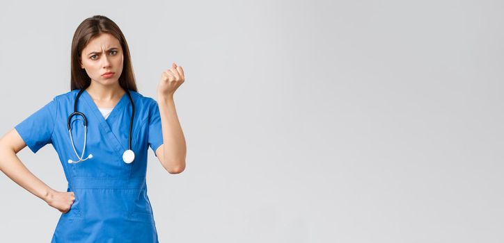 Medical workers, healthcare, covid-19 and vaccination concept. Angry and grumpy young female nurse, doctor scolding young patient breaking quarantine rules, shaking fist in threat.