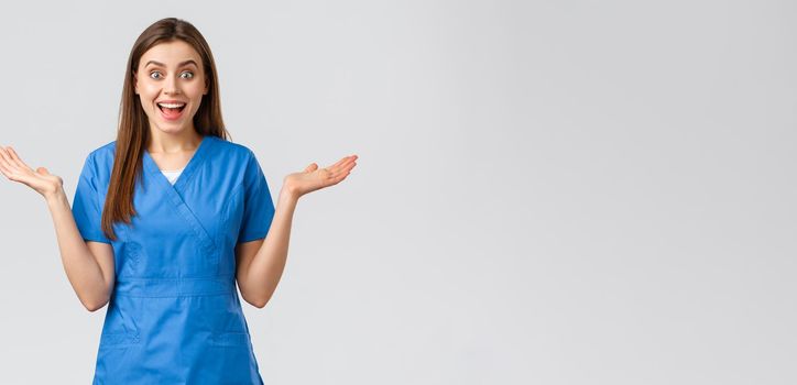 Healthcare workers, prevent virus, insurance and medicine concept. Surprised happy female nurse or doctor hear wonderful news, clap hands open mouth and look fascinated, grey background.