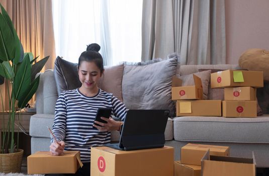 Online Marketing, Young start up small business owner writing address on cardboard box from list order. small business entrepreneur SME or freelance asian woman working with box at home.