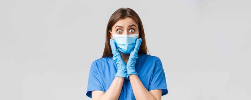 Covid-19, preventing virus, health, healthcare workers and quarantine concept. Close-up of shocked and surprised female nurse or doctor in blue scrubs, medical mask, gasping astonished big news.
