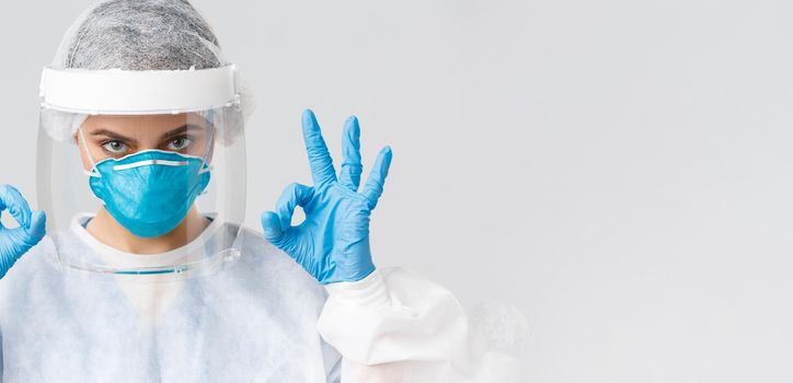 Covid-19, preventing virus, health, healthcare workers and quarantine concept. Close-up serious, determined female doctor or nurse in personal protective equipment, face mask and gloves, show okay.