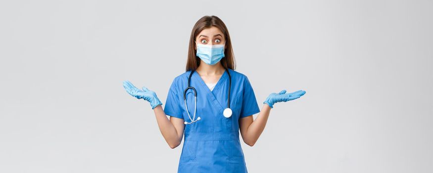 Covid-19, preventing virus, health, healthcare workers and quarantine concept. Surprised and excited female nurse or doctor in blue scrubs and medical mask, spread hands sideways amused.