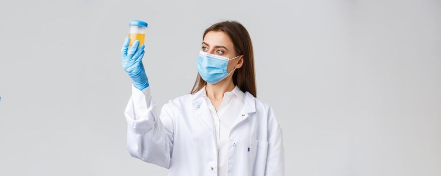 Covid-19, medical research, diagnosis, healthcare workers concept. Professional doctor in clinic lab, scrubs and medical mask, looking at urine sample, patient test on coronavirus infection.