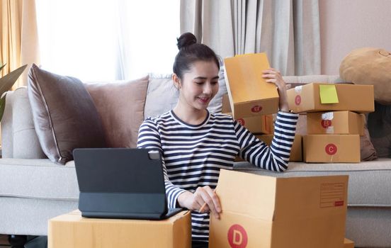 Online Marketing, Young start up small business owner writing address on cardboard box from list order. small business entrepreneur SME or freelance asian woman working with box at home.