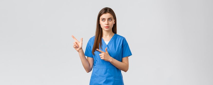 Healthcare workers, prevent virus, insurance and medicine concept. Dreamy cute nurse or doctor in blue scrubs, looking and pointing upper left corner, reading banner info, grey background.