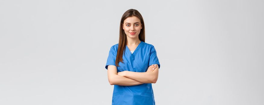 Healthcare workers, prevent virus, insurance and medicine concept. Confident smiling female nurse, doctor in blue scrubs, cross arms chest and look determined. Fighting covid-19 outbreak, stay home.