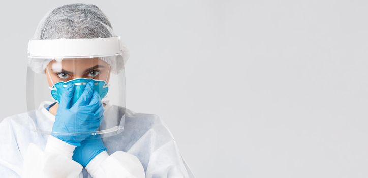 Covid-19, preventing virus, health, healthcare workers and quarantine concept. Close-up serious female doctor, nurse in personal protective equipment, put on respirator, look camera determined.