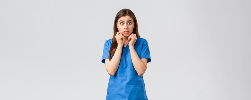 Healthcare workers, prevent virus, insurance and medicine concept. Concerned and scared female nurse hear bad rumor or shocking gossip, trembling, look worried, hold hands near mouth.