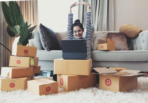 Happy successful business woman with arms up working with laptop and cardboard box on table in home office. business online and delivery concept..