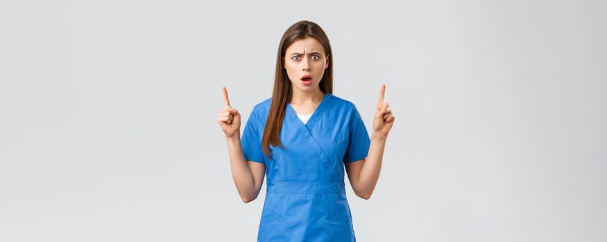 Healthcare workers, prevent virus, insurance and medicine concept. Oh gosh what this. Shocked and concerned nurse or doctor in blue scrubs, frowning upset, gasping pointing fingers up.