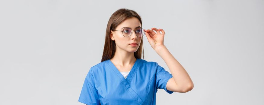 Healthcare workers, medicine, insurance and covid-19 pandemic concept. Professional young smart doctor or nurse, female intern in scrubs and glasses, looking right at banner serious face.