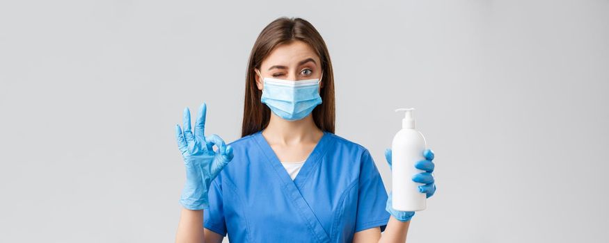 Covid-19, preventing virus, healthcare workers and quarantine concept. Confident cute female nurse or doctor in blue scrubs, medical mask and gloves, approve and recommend soap or hand sanitizer.