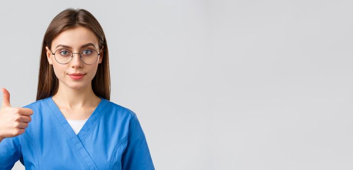 Healthcare workers, medicine, insurance and covid-19 pandemic concept. Close-up supportive and confident female nurse, doctor in blue scrubs and glasses, show approval thumbs-up, guarantee.