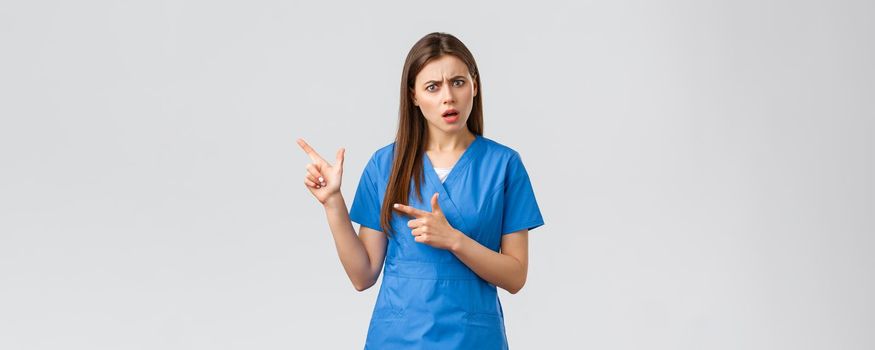 Healthcare workers, prevent virus, insurance and medicine concept. Concerned and puzzled nurse or doctor look confused, pointing fingers left, need answer, asking question, grey background.