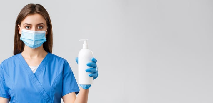 Covid-19, preventing virus, health, healthcare workers and quarantine concept. Serious-looking medical worker, nurse or doctor in blue scrubs and medical mask, showing hand sanitizer or soap.