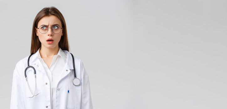 Healthcare workers, medicine, insurance and covid-19 pandemic concept. Shocked and confused young female doctor in white scrubs and glasses, stethoscope, stare left with concerned nervous face.