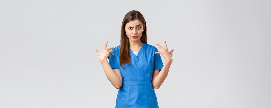 Healthcare workers, prevent virus, insurance and medicine concept. Funny displeased female nurse in blue scrubs grimacing, freak out over something, mimicking and staring camera shocked.