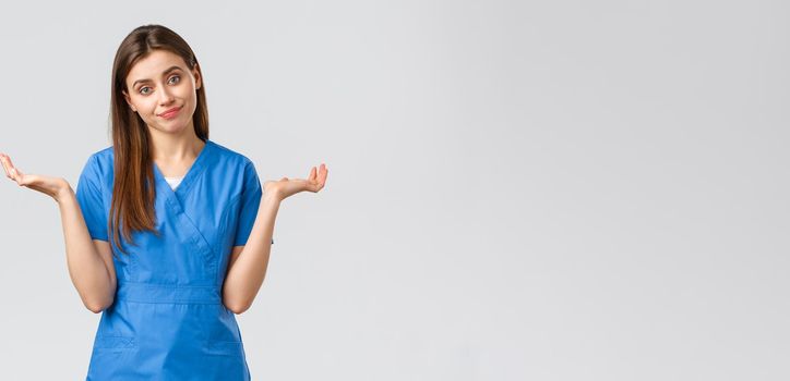 Healthcare workers, prevent virus, insurance and medicine concept. Doctor shrugging as cant tell, have no idea, sorry dont know. Female nurse in blue scrubs spread hands sideways.