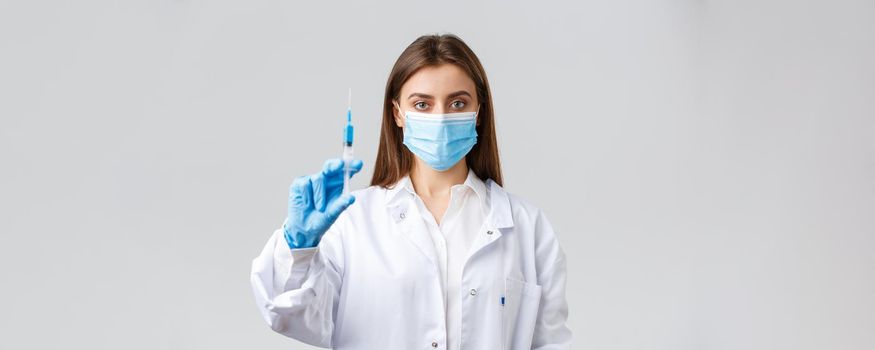 Covid-19, preventing virus, healthcare workers and quarantine concept. Determined professional doctor in medical mask and rubber gloves, showing syringe filled with coronavirus vaccine.