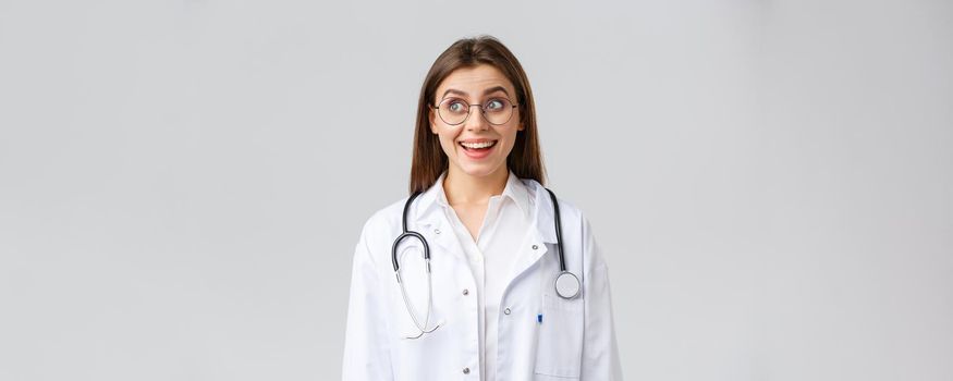 Healthcare workers, medicine, insurance and covid-19 pandemic concept. Happy optimistic female doctor, physician with stethoscope in white scrubs and glasses, look upper left corner with upbeat smile.