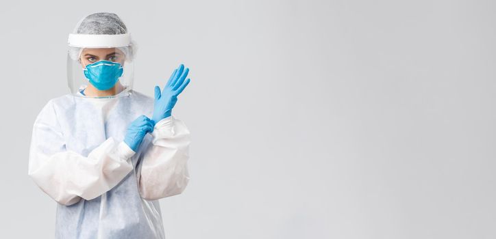 Covid-19, preventing virus, health, healthcare workers and quarantine concept. Serious female doctor in personal protective equipment PPE, shield, face mask out on gloves to enter patient room.