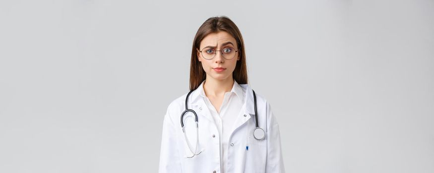 Healthcare workers, medicine, insurance and covid-19 pandemic concept. Skeptical and confused female doctor in white scrubs, medical suit and glasses, raise eyebrow judgemental, smirk displeased.