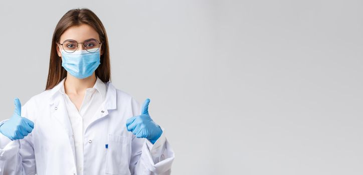 Covid-19, preventing virus, healthcare workers and quarantine concept. Cheerful female doctor, physician in white scrubs and rubber gloves, show thumb-up, ask use protection against corona infection.
